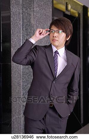 Stock Photograph - Young businessman looking away and holding glasses. Fotosearch
