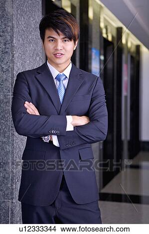 Young businessman standing with hands on chest and smiling at the camera View Large Photo Image Picture - Young businessman standing with hands on chest and smiling at the camera. Fotosearch