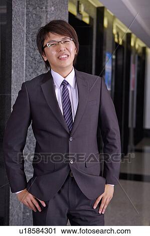 Young businessman standing with hands in pockets and smiling at the camera View Large Photo Image Stock Image - Young businessman standing with hands in pockets and smiling at the camera. Fotosearch
