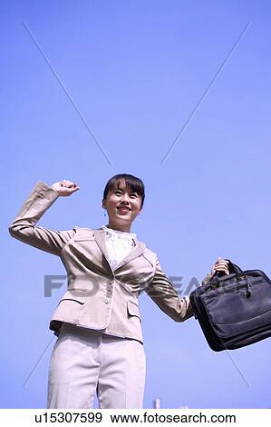 Stock Photo - Young woman standing with fist up and holding briefcase with smile. Fotosearch