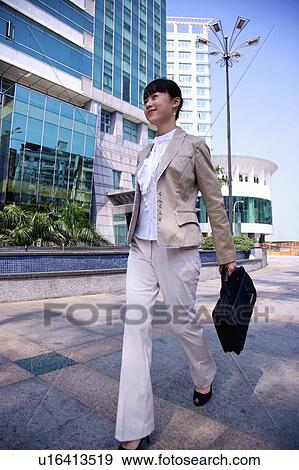 Stock Photo - Young woman walking and holding briefcase with smile. Fotosearch
