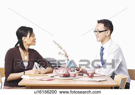 Stock Image - Businessman and a businesswoman sitting on chairs looking at each other. Fotosearch