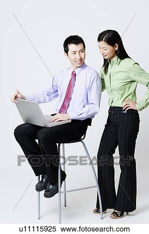 Stock Photography - Businessman holding a laptop with a businesswoman standing beside him. Fotosearch
