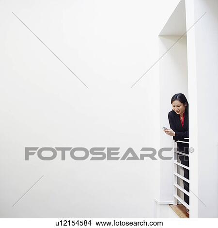 Picture - Businesswoman leaning over a railing and operating a mobile phone. Fotosearch