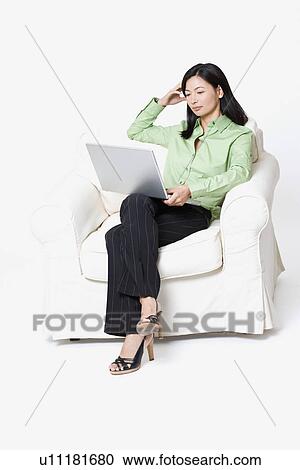 Businesswoman sitting in an armchair and using a laptop View Large Photo Image Stock Image - Businesswoman sitting in an armchair and using a laptop. Fotosearch