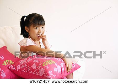 Stock Photo - Close-up of a girl sitting on a couch and eating a lollipop. Fotosearch