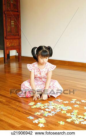 Stock Image - Close-up of a girl sitting on the floor and playing with a jigsaw puzzle. Fotosearch