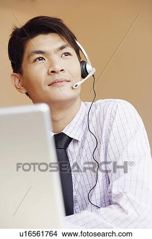 Close-up of a male customer service representative talking on a headset and thinking View Large Photo Image Picture - Close-up of a male customer service representative talking on a headset and thinking. Fotosearch