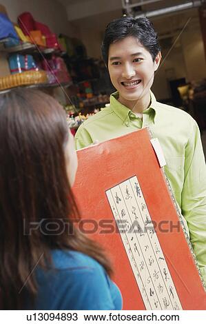 Stock Image - Close-up of a young couple holding a painting in a store. Fotosearch