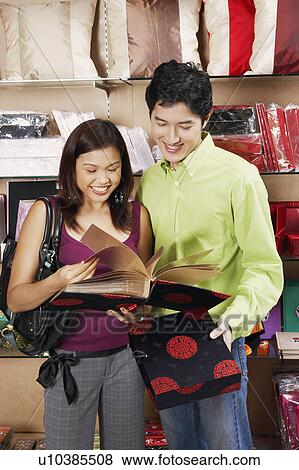 Close-up of a young couple holding a photo album in a store View Large Photo Image Stock Photo - Close-up of a young couple holding a photo album in a store. Fotosearch