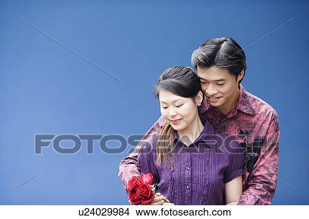 Close-up of a young man embracing a young woman from behind and holding roses View Large Photo Image Picture - Close-up of a young man embracing a young woman from behind and holding roses. Fotosearch