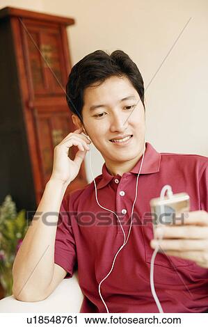 Stock Image - Close-up of a young man listening to an MP3 player and smiling. Fotosearch