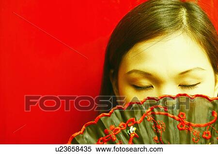 Stock Photography - Close-up of a young woman covering her mouth with a folding fan. Fotosearch