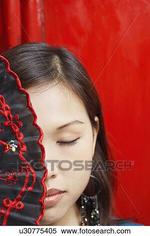 Stock Photography - Close-up of a young woman covering her one eye with a folding fan. Fotosearch