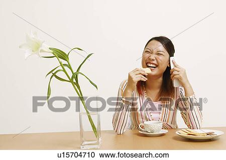 Stock Image - Close-up of a young woman eating a cookie and talking on a mobile phone. Fotosearch
