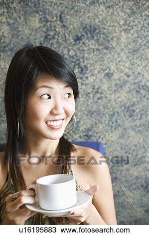 Close-up of a young woman holding a cup of coffee and looking away in a restaurant View Large Photo Image Stock Image - Close-up of a young woman holding a cup of coffee and looking away in a restaurant. Fotosearch