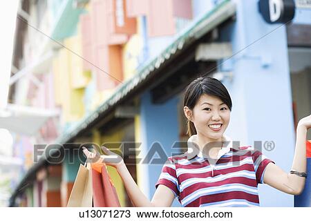 Stock Image - Close-up of a young woman holding shopping bags and smiling. Fotosearch