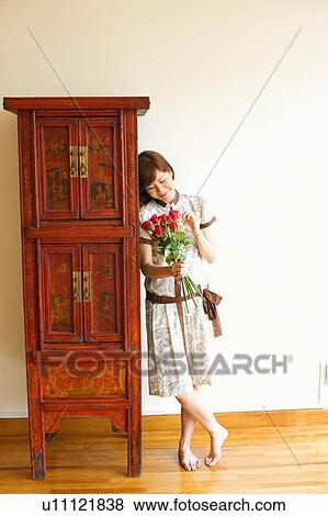 Close-up of a young woman standing near a cabinet and holding a bouquet of red roses View Large Photo Image Stock Photo - Close-up of a young woman standing near a cabinet and holding a bouquet of red roses. Fotosearch