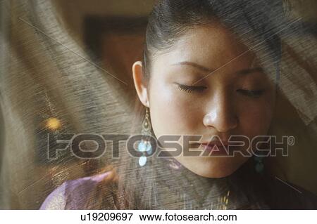 Stock Photo - Close-up of a young woman with her eyes closed hiding behind a transparent curtain. Fotosearch