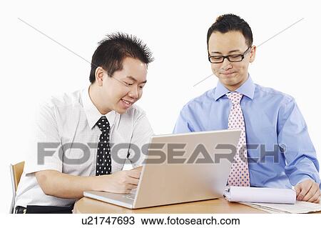 Stock Image - Close-up of two businessmen sitting in front of a laptop. Fotosearch