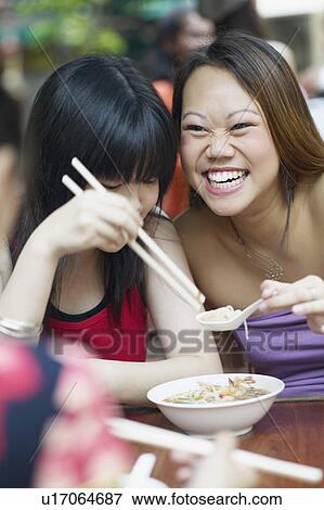 Stock Photo - Close-up of two young women eating noodles with chopsticks. Fotosearch