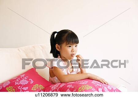 Stock Photo - Girl sitting on a couch and eating a lollipop. Fotosearch