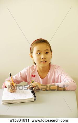 Stock Image - Girl writing on a spiral notebook in the classroom. Fotosearch
