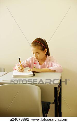 Stock Image - Girl writing on a spiral notebook in the classroom. Fotosearch