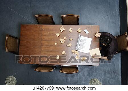 Stock Photo - High angle view of a businessman writing on a notepad with crushed papers on the table. Fotosearch