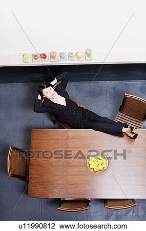 Stock Image - High angle view of a businesswoman reclining and resting her feet on the table. Fotosearch