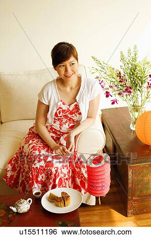 Stock Photograph - High angle view of a young woman sitting on a couch and holding a Chinese lantern. Fotosearch