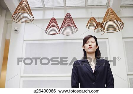 Stock Photograph - Low angle view of a businesswoman standing with her eyes closed. Fotosearch