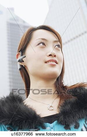 Stock Photograph - Low angle view of a young woman wearing a hands free device. Fotosearch