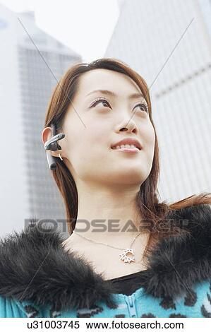 Stock Photography - Low angle view of a young woman wearing a hands free device. Fotosearch