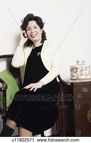 Stock Image - Mature woman sitting on a chair talking on a mobile phone. Fotosearch