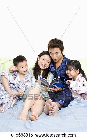 Mid adult man and a young woman reading a book on the bed with their children View Large Photo Image Stock Photography - Mid adult man and a young woman reading a book on the bed with their children . Fotosearch
