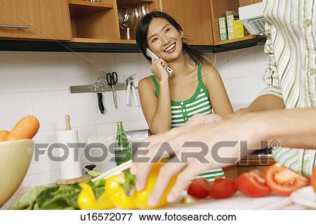 Mid section view of a man cutting vegetables with a young woman talking on a mobile phone in the kitchen View Large Photo Image Stock Photo - Mid section view of a man cutting vegetables with a young woman talking on a mobile phone in the kitchen. Fotosearch