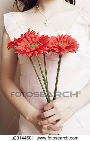 Stock Image - Mid section view of a young woman holding flowers. Fotosearch