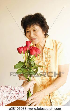 Stock Image - Person offering a bunch of roses to a mature woman. Fotosearch