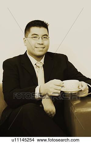 Picture - Portrait of a businessman sitting on a couch with a cup of tea and smiling. Fotosearch
