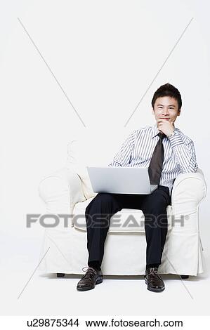 Picture - Portrait of a businessman sitting with a laptop on his lap. Fotosearch