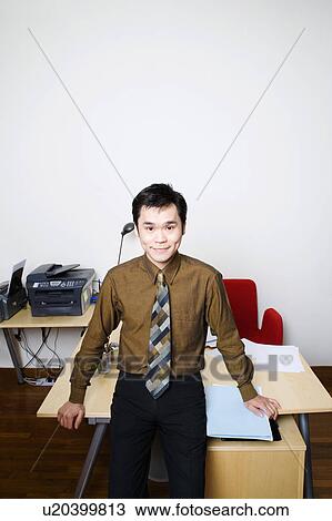 Stock Image - Portrait of a businessman smiling and standing in an office. Fotosearch