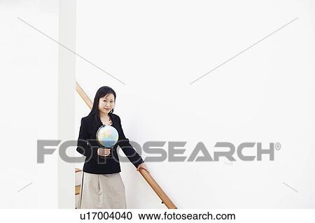Stock Image - Portrait of a businesswoman holding a globe and standing on the staircase. Fotosearch