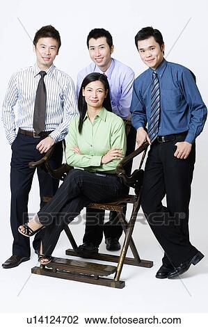 Stock Image - Portrait of a businesswoman sitting with three businessmen standing beside her. Fotosearch