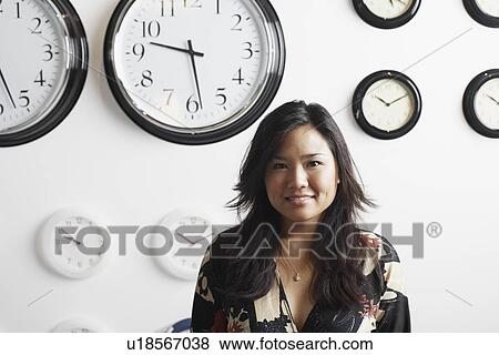 Portrait of a businesswoman standing in front of clocks on the wall View Large Photo Image Stock Photo - Portrait of a businesswoman standing in front of clocks on the wall. Fotosearch