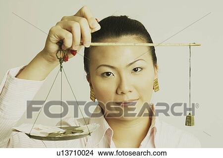 Picture - Portrait of a businesswoman weighing paper currency with coins on a weighing scale. Fotosearch