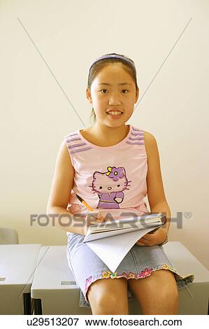 Portrait of a girl sitting on the desk and writing on a spiral notebook View Large Photo Image Stock Photo - Portrait of a girl sitting on the desk and writing on a spiral notebook. Fotosearch