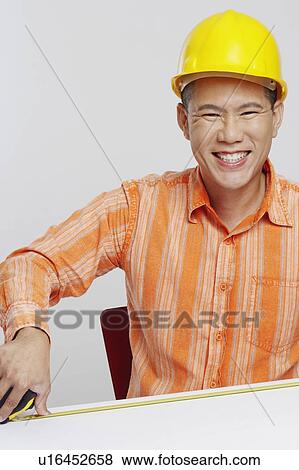 Portrait of a male architect measuring a desk with a tape measure and smiling View Large Photo Image Stock Photo - Portrait of a male architect measuring a desk with a tape measure and smiling. Fotosearch