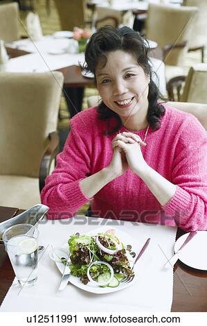 Stock Image - Portrait of a mature woman seated at the table in a restaurant smiling. Fotosearch