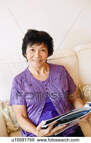 Portrait of a mature woman sitting on a couch and holding a magazine View Large Photo Image Stock Photo - Portrait of a mature woman sitting on a couch and holding a magazine. Fotosearch